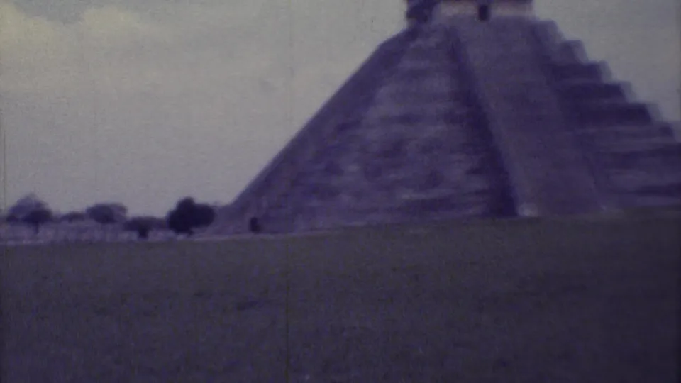 1973 8mm home-movie view of El Castillo at Chichen Itza, seen across grass under a muted sky.