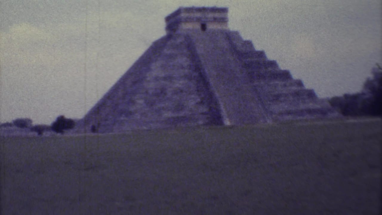 Stepped pyramid with temple top seen across open grass.