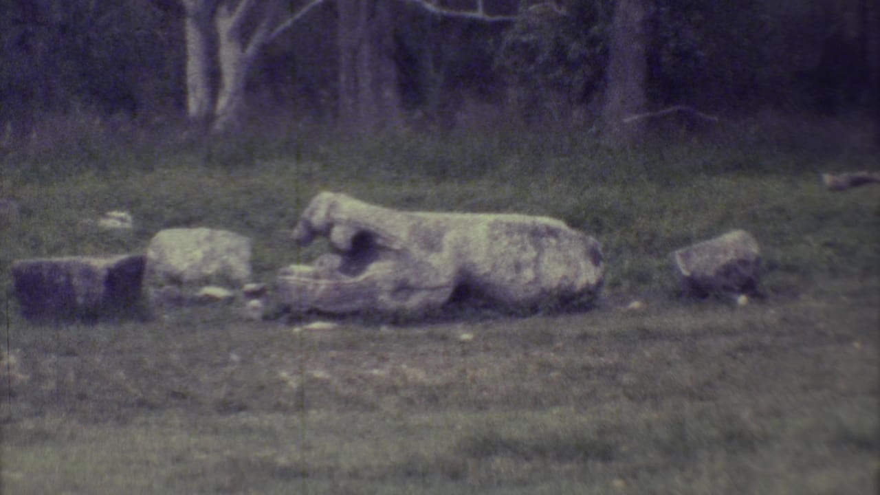 Reclining stone sculpture beside stone blocks on a grassy slope.