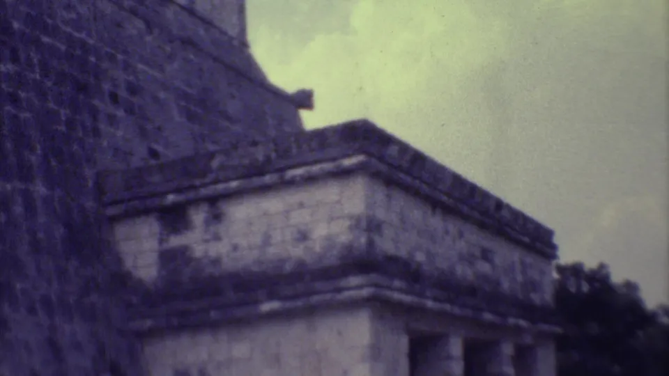 Soft 8mm frame from Yucatan showing a stepped stone wall and a lower weathered ruin structure beneath cloudy sky.