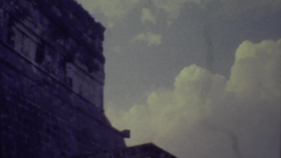 The camera continues past a dark stone structure, showing block masonry and clouds in 1973 Yucatan home-movie footage.