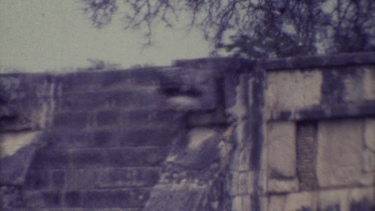 Close view of a weathered stone ruin with stepped masonry and trees behind it.