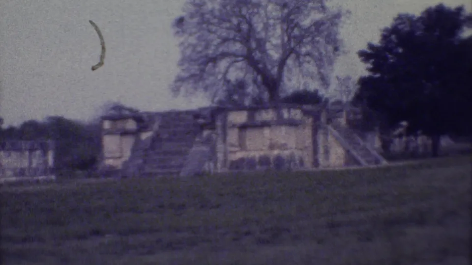 Final 1973 Yucatan frame holds on the stone ruin and steps, with grass, trees, and a visible film mark near the sky area.