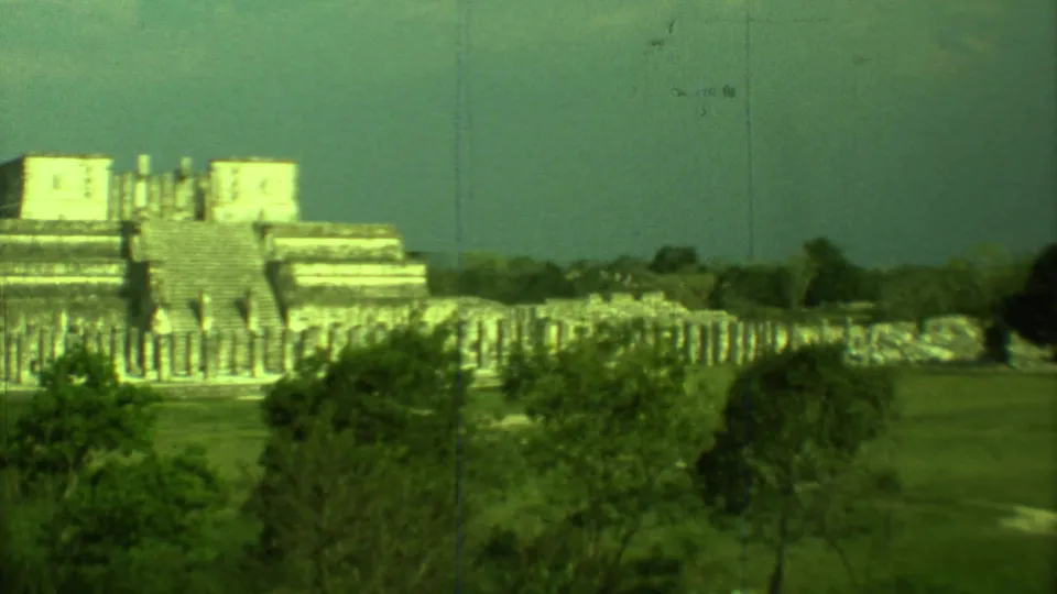 1973 Yucatan home-movie frame showing Chichen Itza ruins, column-like stones, trees, and open grass during a pan.
