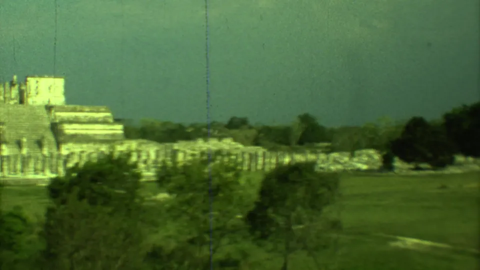 Late frame of the 1973 8mm pan across Chichen Itza, with the stepped temple, surrounding ruins, trees, and open grounds visible.