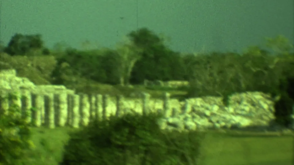 Soft 8mm frame from Yucatan, Mexico showing pale Mayan stone ruins, trees and open grass during a slow pan.