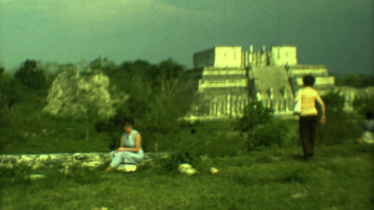 Tourists in a grassy area with a stepped stone ruin in the background.