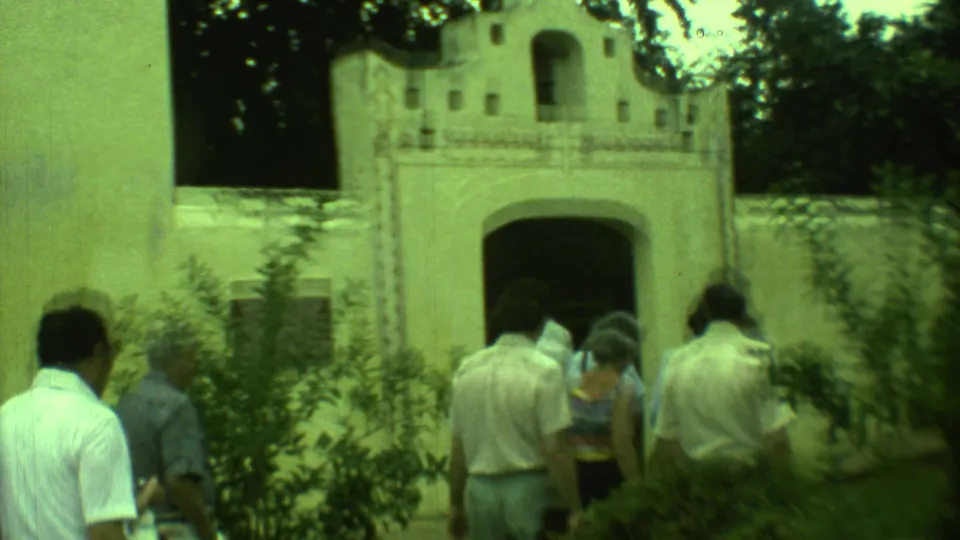 1973 Yucatan frame showing visitors walking toward a white colonial-style building with arched openings and decorative trim.