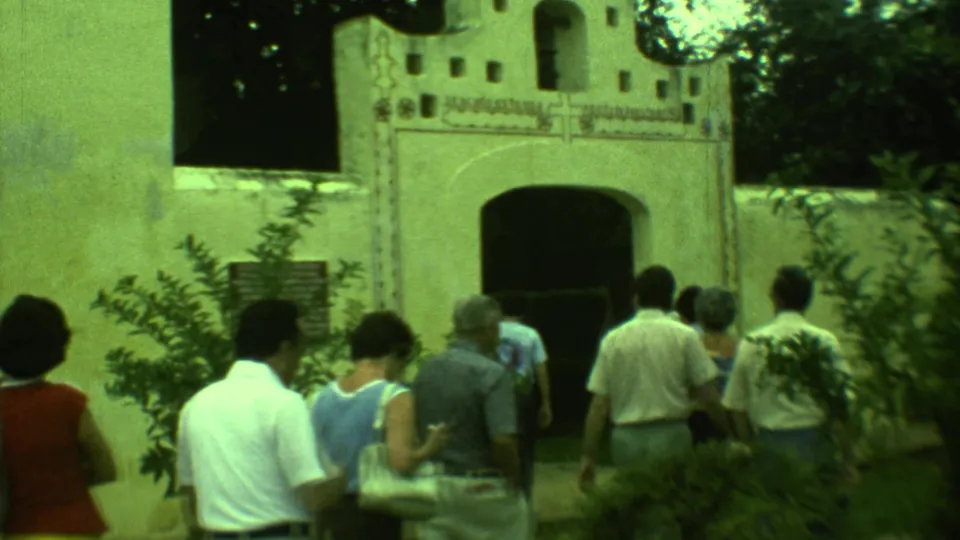 1973 Yucatan home-movie frame of tourists in casual dress approaching a white arched building through surrounding vegetation.