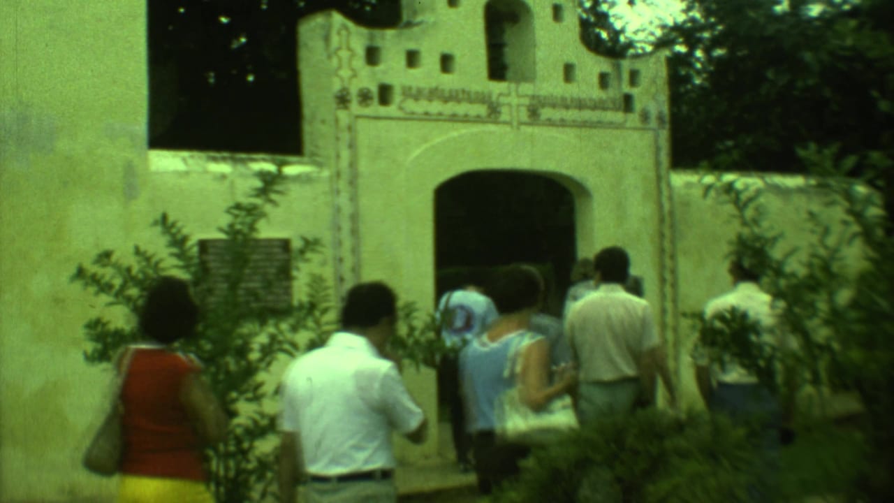 1973 Yucatan 8mm frame showing adults walking toward a white stucco church facade with arched openings and trees.