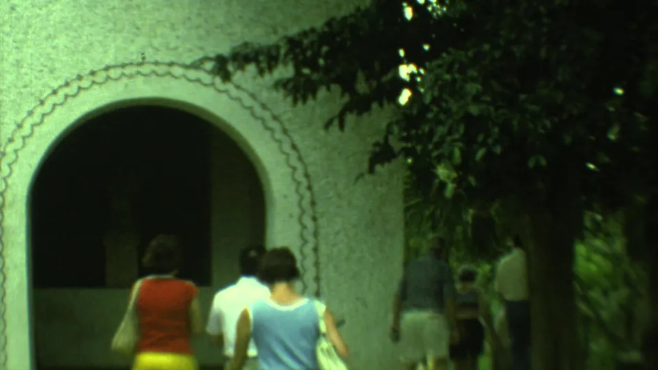 1973 Yucatan frame with adults seen from behind near a large white stucco arch and shaded church doorway.