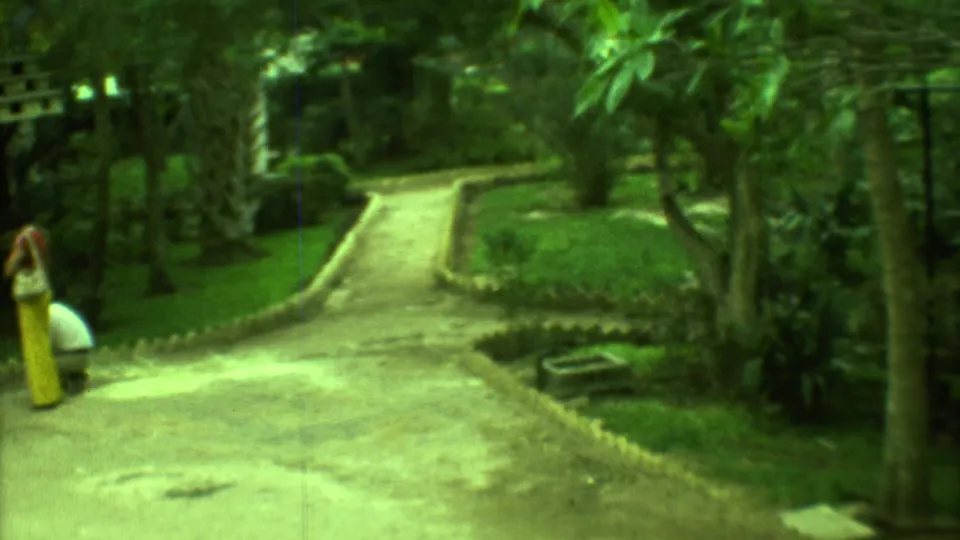 1973 Yucatan home-movie frame showing a distant person in yellow near a winding path and tropical mini golf landscaping.