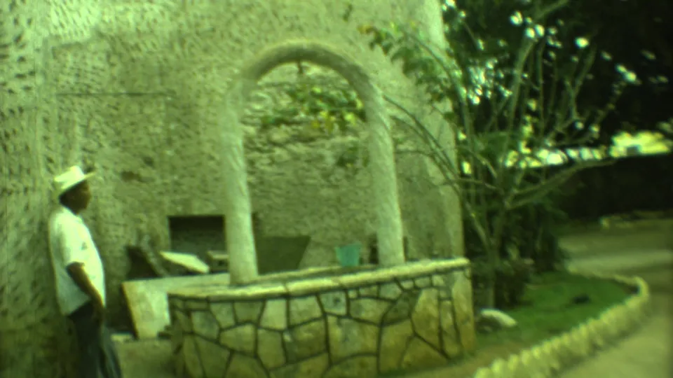 Yucatan 1973 home-movie frame showing a hat-wearing man near a stone arch or well-like garden structure.