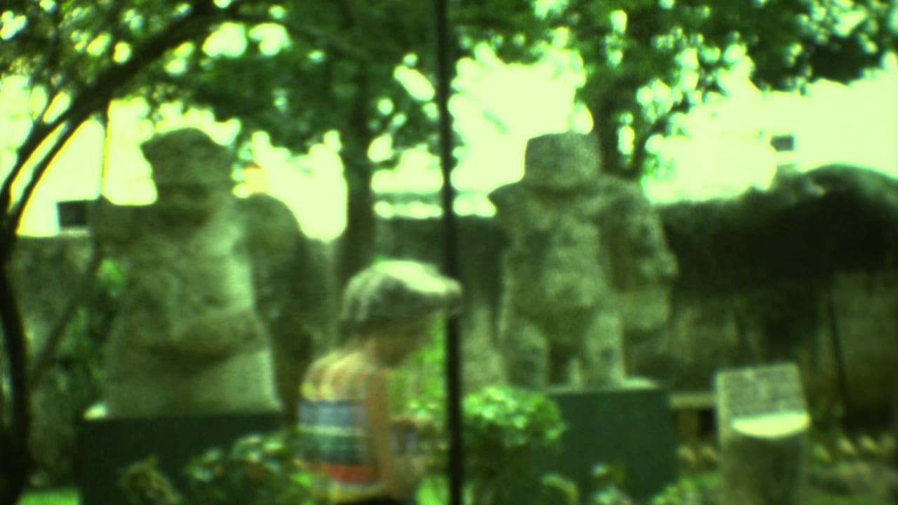 Tourists stand near large carved stone figures in a shaded garden exhibit.