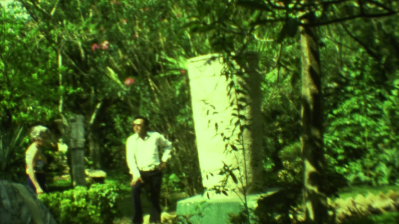 Tourists standing near pale stone monuments in a leafy ruin setting.