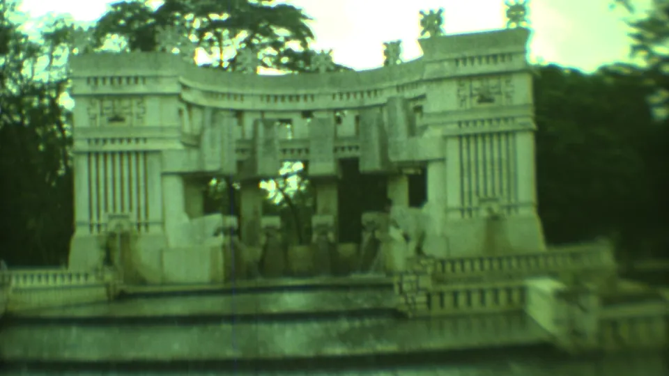1973 Yucatan 8mm frame showing a carved fountain-like stone facade near a low masonry building, shrubs, and trees.
