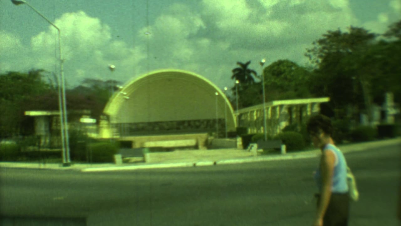 Arched pavilions, benches, palms, and a woman walking along a road in a park.