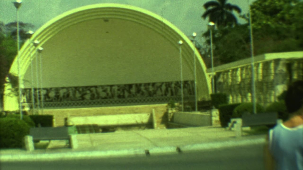 Large arched pavilion beside benches, shrubs, and pedestrians at the edge of the frame.