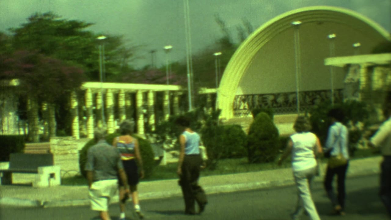 Small group walking toward a large curved dome structure beside shrubs and lampposts.