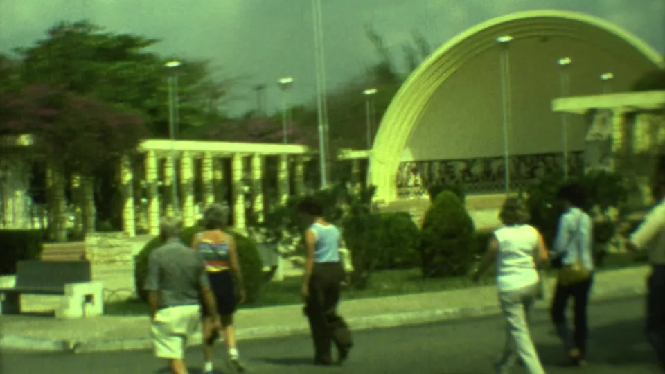 1973 Yucatan home-movie frame showing visitors walking along a paved path toward a large curved outdoor dome structure.
