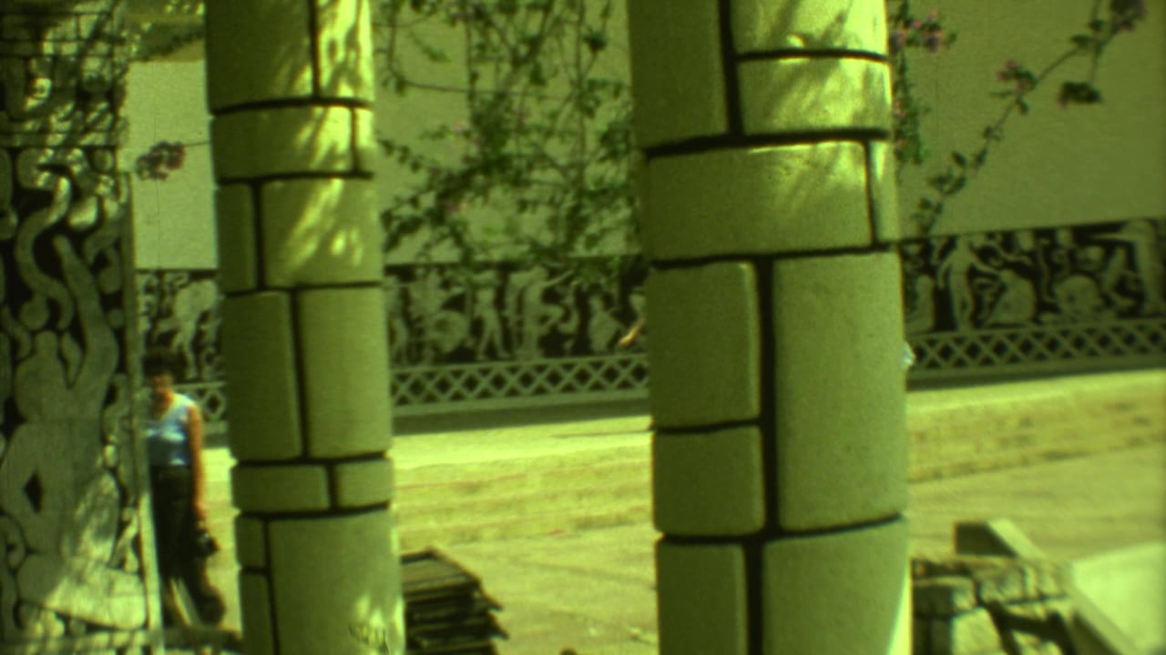 Stone columns frame a decorative mural wall beside a paved public area.