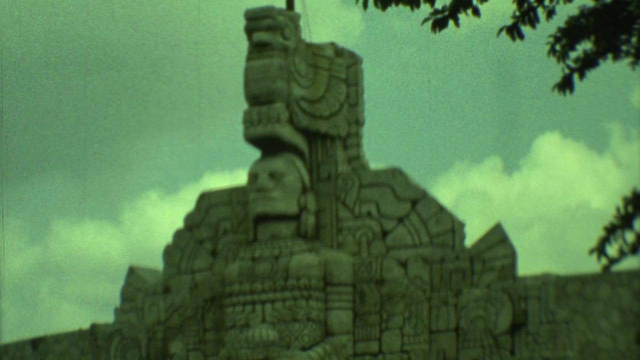 Close view of a carved stone figure rising above patterned stonework under a cloudy sky.