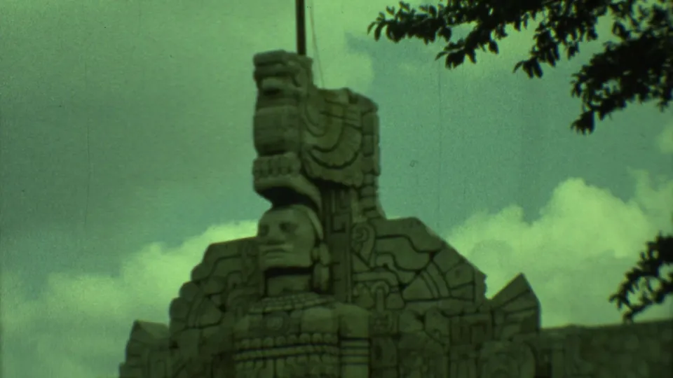 1973 Yucatan home-movie frame of a carved stone monument, with a figure form and decorative stone patterns under branches.