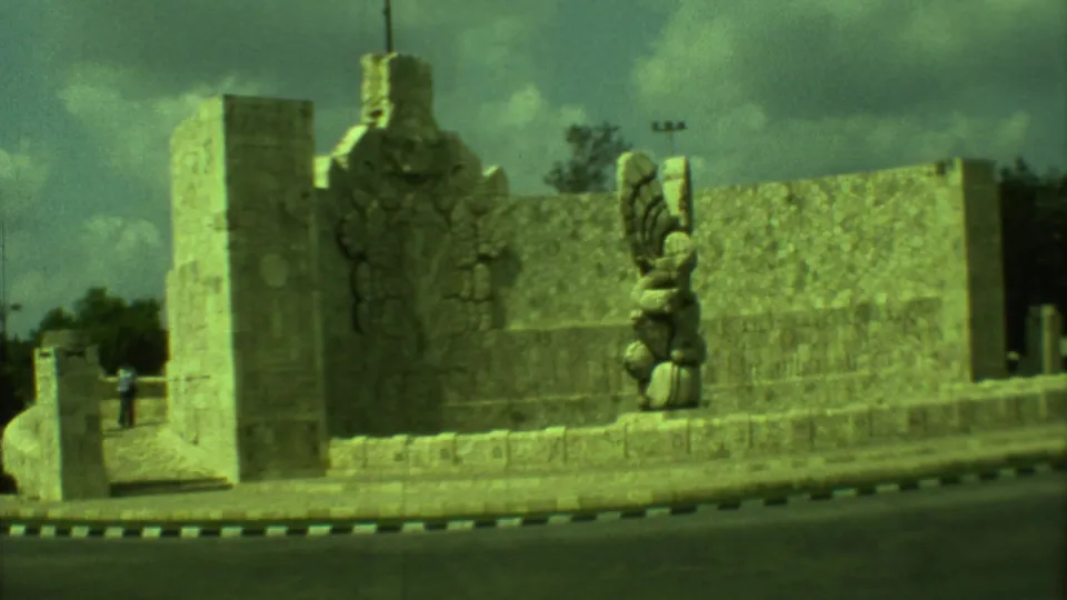 Yucatán, Mexico, 1973 home-movie frame showing the stone roundabout monument from a moving viewpoint, with carvings and trees behind it.