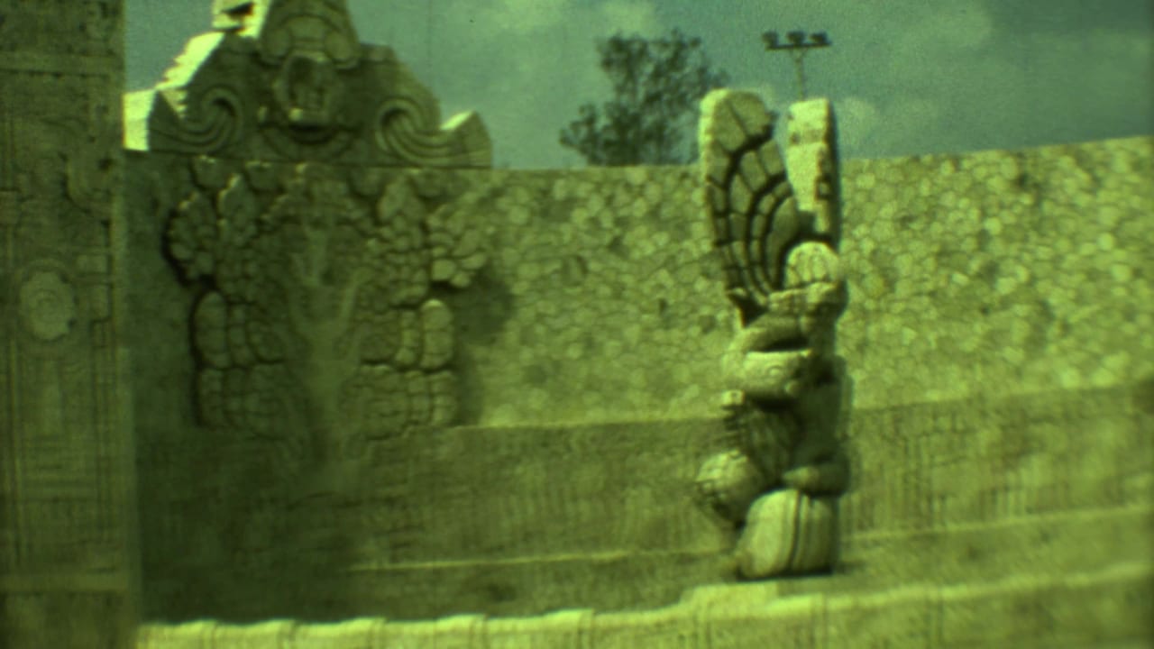 Wide view of carved stone figures beside a patterned stone wall.