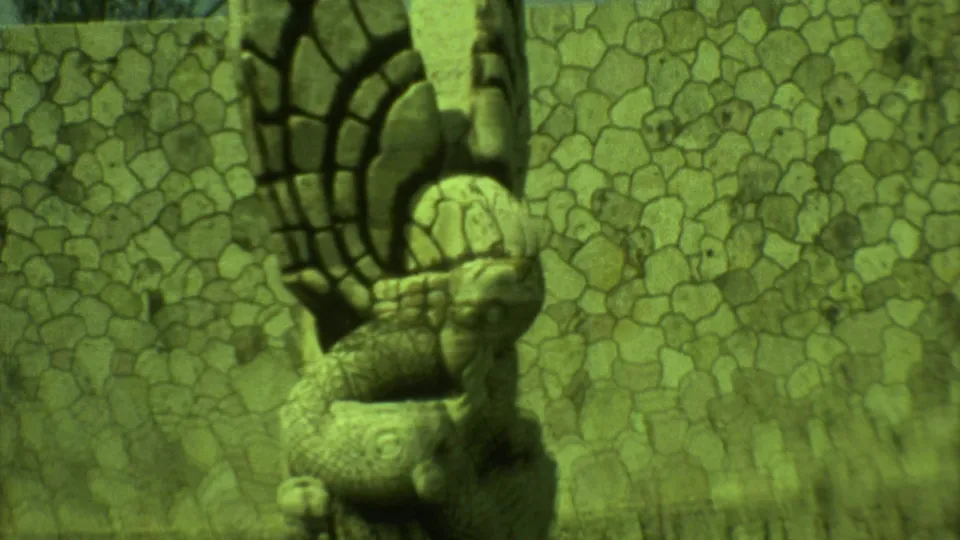 1973 Yucatan 8mm close-up of a serpent-like carved stone figure with patterned wall stones behind it.