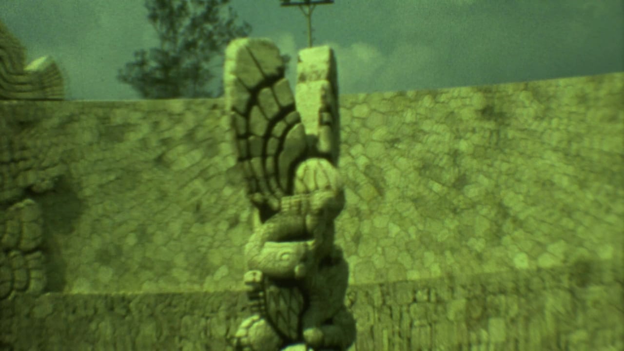Stone carved figure beside a textured wall under a cloudy sky.