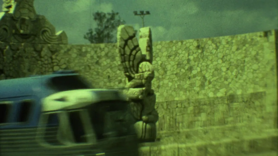 A blue and white bus moves past the stone monument in 1973 Yucatan home-movie footage.