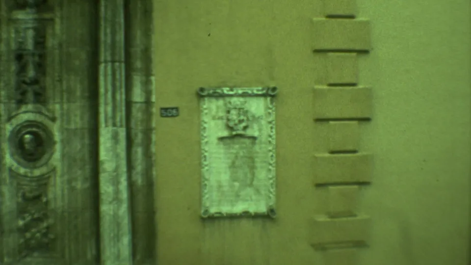1973 Yucatan 8mm frame showing a weathered wall plaque beside carved stone architectural details on a town street.