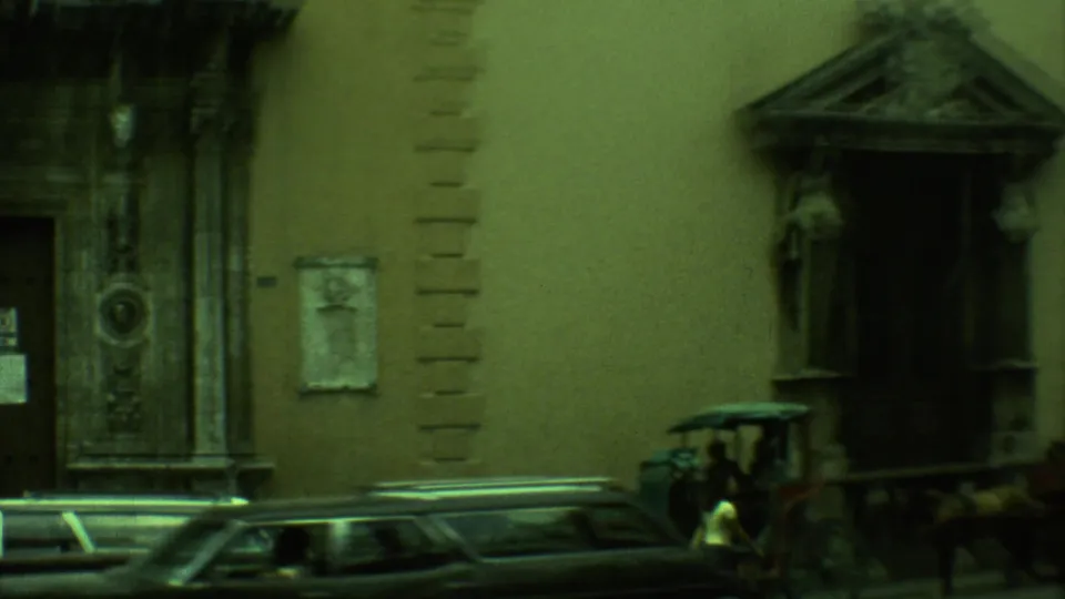Yucatan, Mexico street view from 1973 with ornate stone entrances, a dark car, and a horse-drawn carriage near the curb.