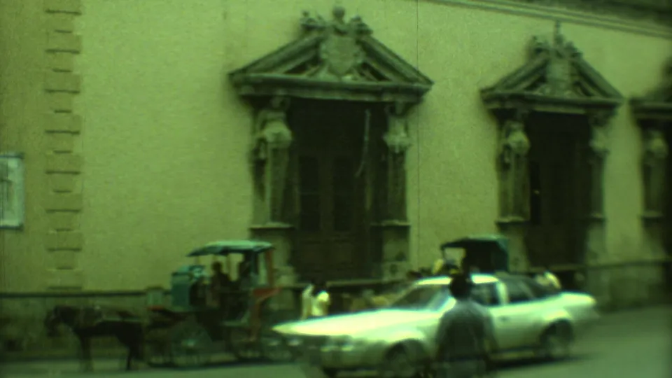 1973 Yucatan street frame with a carriage, a light-colored classic car, and carved doorway surrounds on a colonial-style facade.
