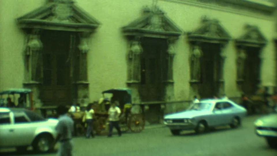 Wide 1973 Yucatan town street view with pedestrians, carriages, classic cars, and repeated carved stone entrances.