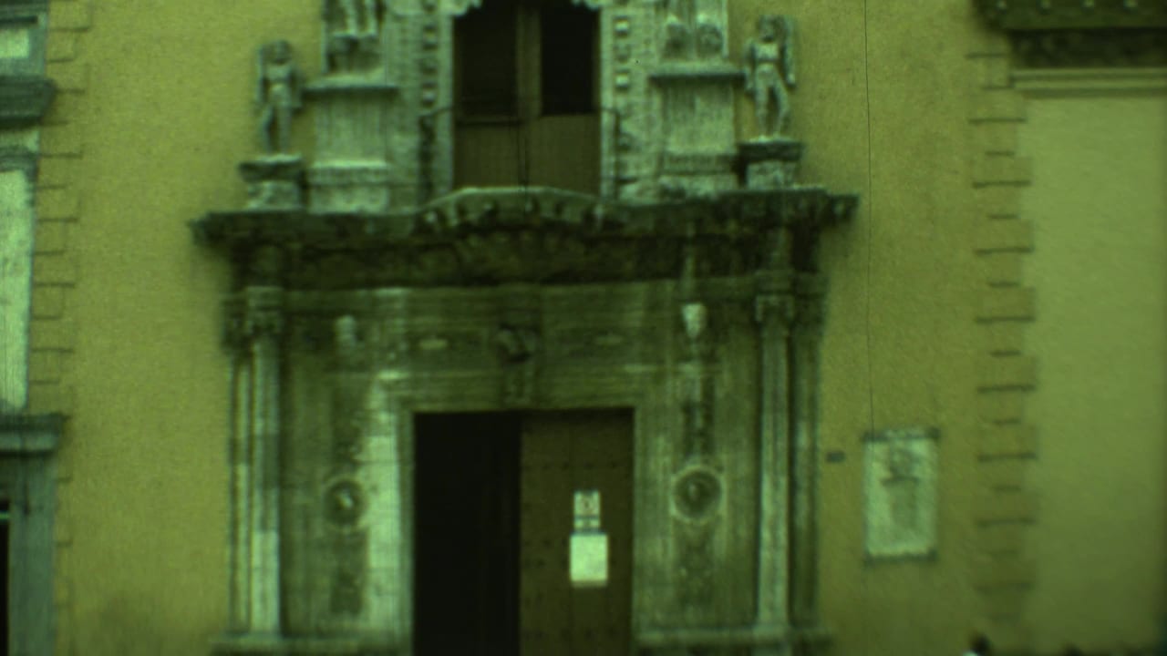 Ornate stone entrance on a stucco building with carved figures and an open doorway.