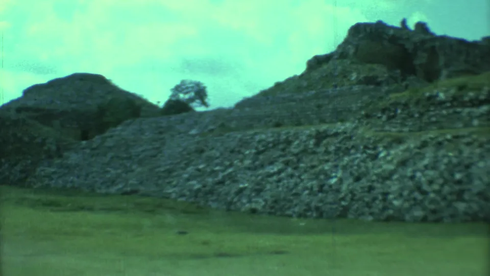 1973 8mm frame from Yucatan showing a rocky Mayan ruin mound, a lone tree, grass, and a green color shift.