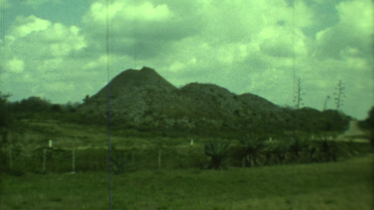 Rocky mounds beyond grass and fencing under a cloudy sky.