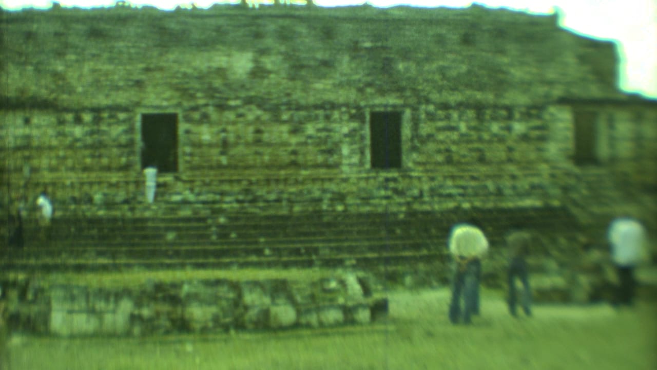 Tourists stand near stepped stone ruins with dark rectangular openings.