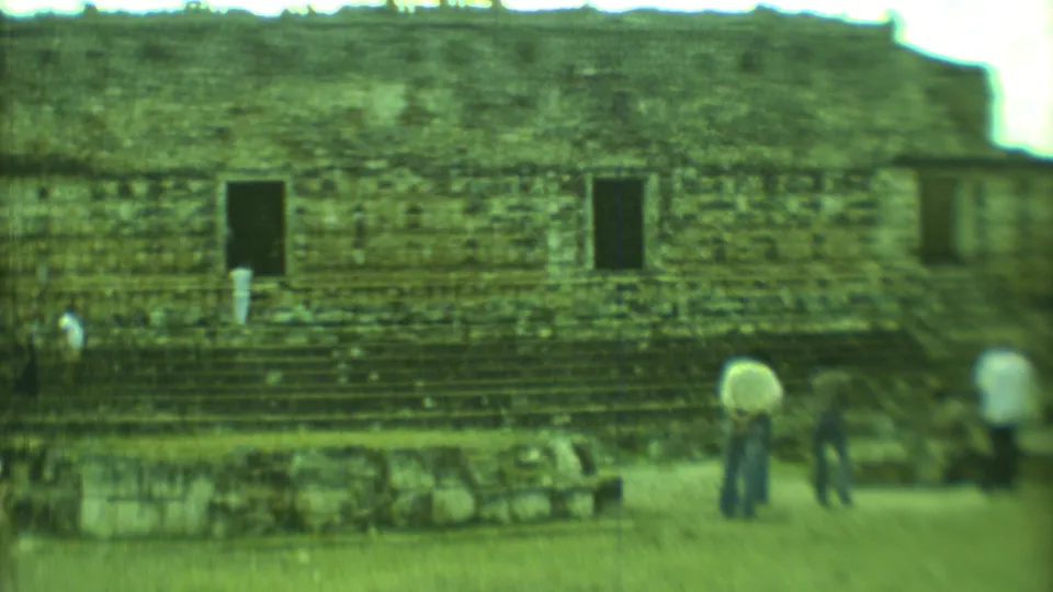 1973 8mm view of tourists exploring stepped Mayan ruins in Yucatan, Mexico, with weathered stone walls and dark openings.