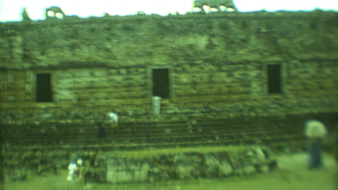 Soft green-tinted 8mm frame of tourists moving beside a weathered Mayan stone structure in Yucatan, Mexico.