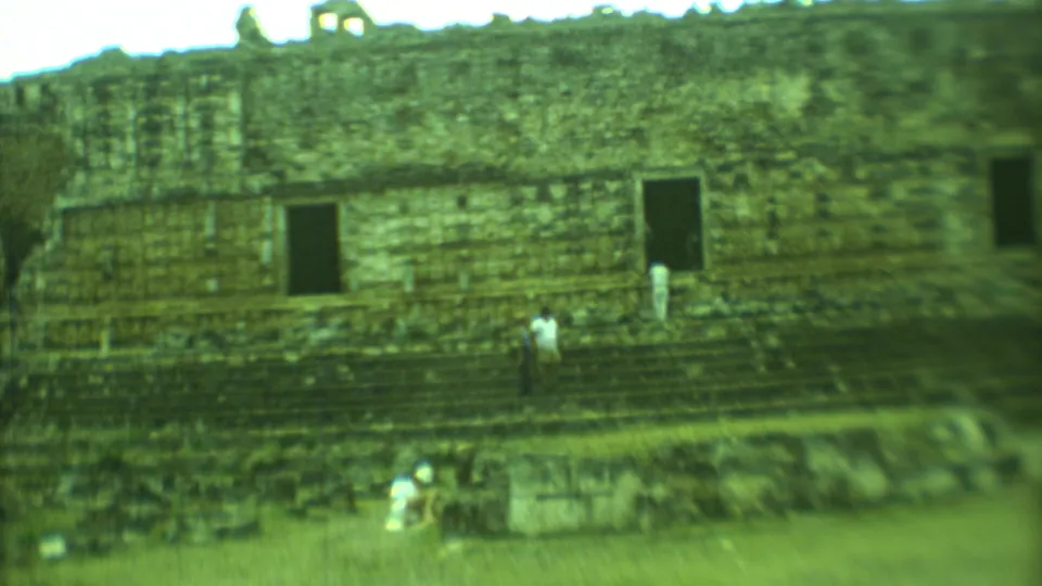 1973 Yucatan home-movie frame showing a visitor on the steps beneath a dark rectangular opening in Mayan ruins.