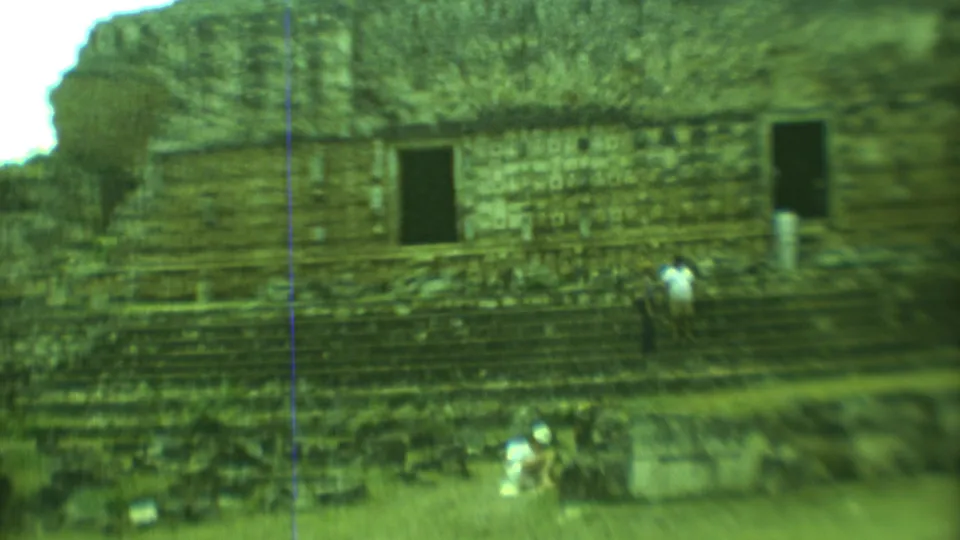 1973 Yucatan travel footage frame with a broad view of a Mayan ruin facade and visitors providing scale near the stairway.