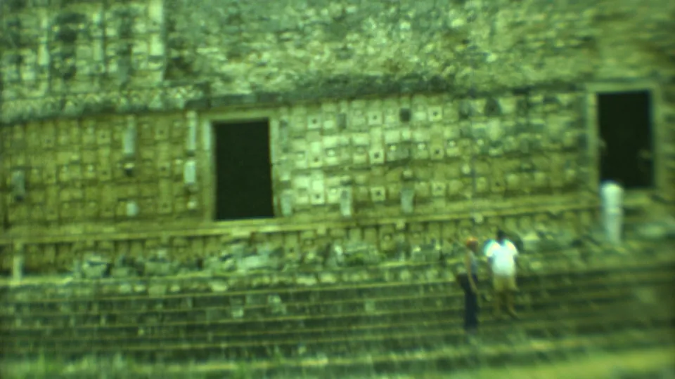 Closer 1973 Yucatan frame showing tourists beside a dark doorway and stepped platform on a weathered Mayan stone structure.