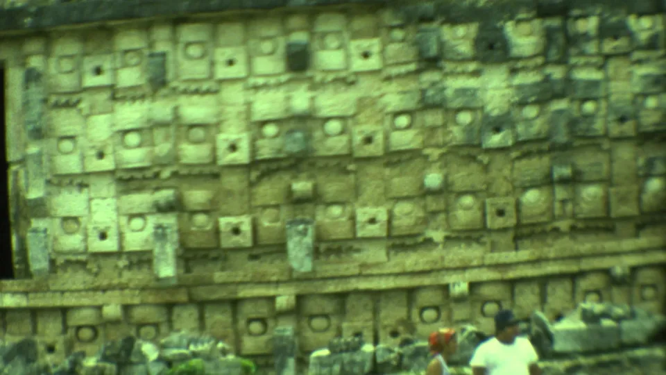 1973 Yucatan home-movie frame emphasizing geometric carved stonework on a Mayan ruin, with visitors partly visible below.