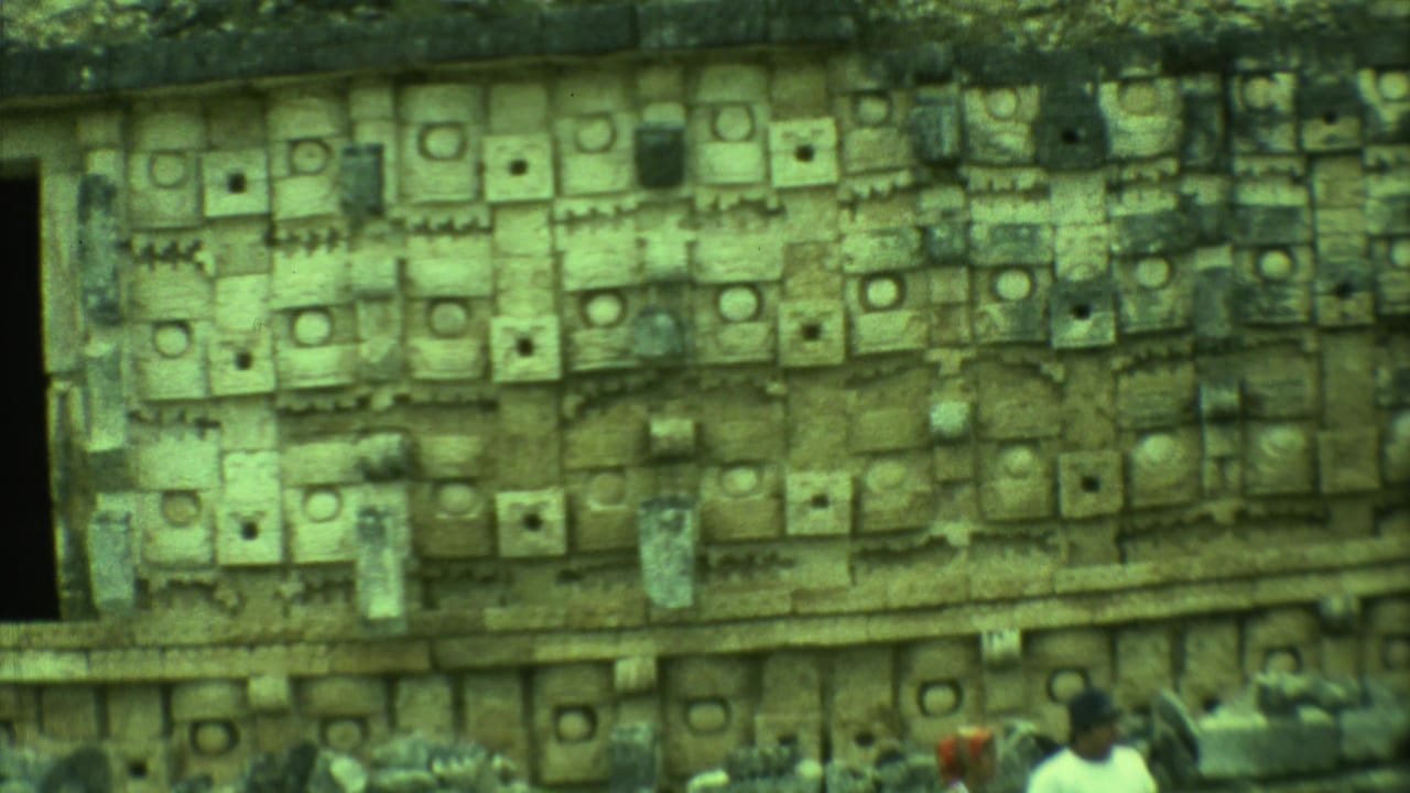 Carved stone wall with geometric panels at a Mayan ruin site.