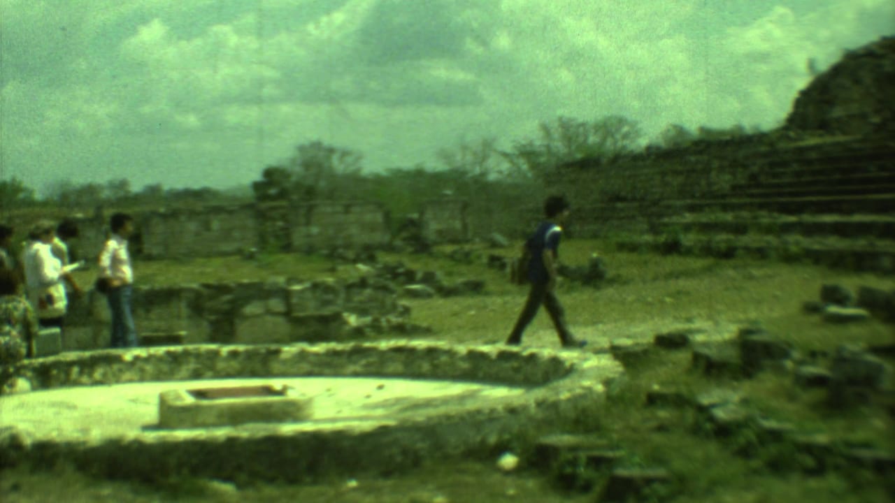 Tourists stand and walk among stone ruins with temple steps in the background.