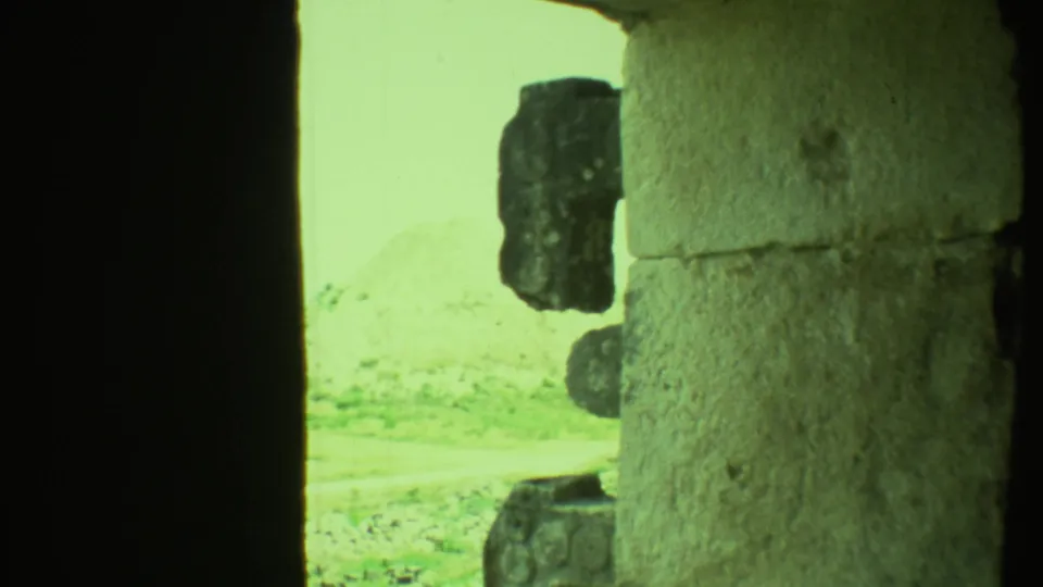 A handheld 8mm view from a shaded stone passage shows weathered masonry and a bright exterior ruin area in Yucatan.