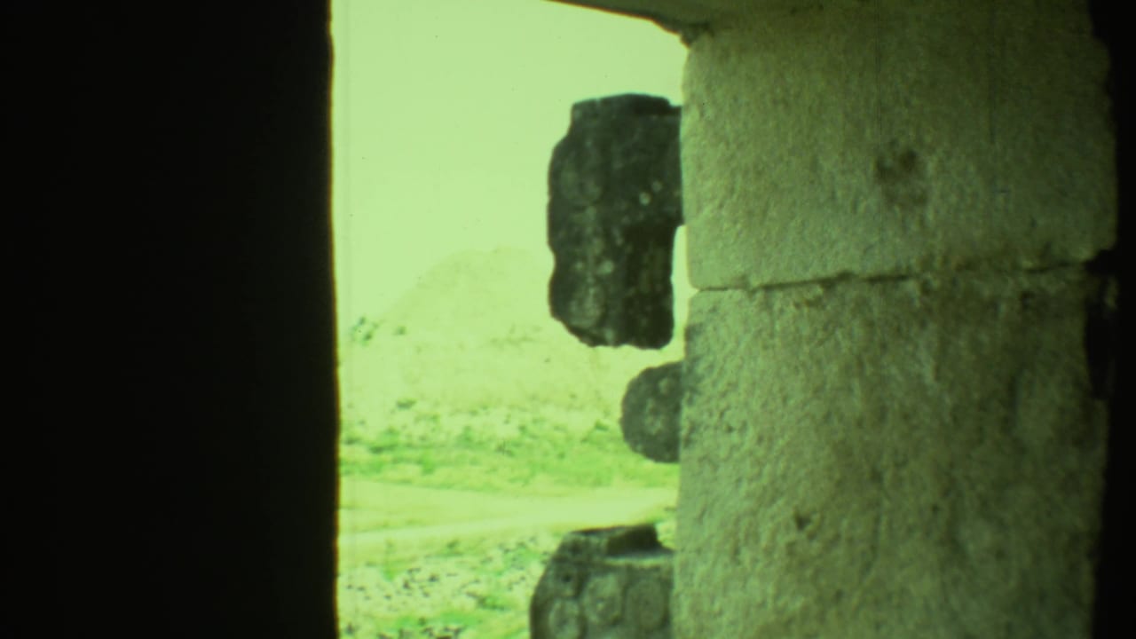 View past a dark stone doorway toward pale ground and rough exterior stonework.